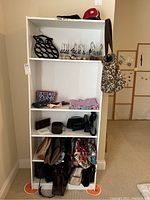 Shelf displaying multiple handbags, belts, cosmetic bags, knit scarf, and metal pants hangers with black owl-shaped circular hanger on upper shelf