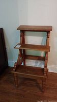 Front view of vintage handmade wooden plant stand showing the three shelves and overall structure.
