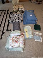Various bedding pieces including king and queen comforters, shams, sheets, and a weighted blanket arranged on carpet with metal bed frame parts.