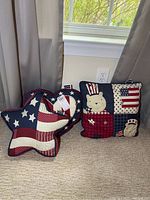 Three patriotic decorative pillows, including one shaped like the US and two square patchwork pillows with bear appliqués and flag patterns.