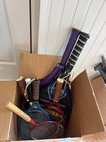 Photo showing multiple rackets with wooden handles in a cardboard box