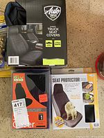 Three different seat covers including a 2-pack Auto Drive truck seat covers, one AV Era black seat cover, and a dog seat protector seat cover.
