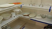 Photo showing multiple ceramic bowls, tureen with ladle, glass and ovenware dishes on shelves.