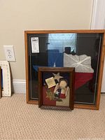 Photo showing two framed shadow box artworks placed on the floor against a wall, one with Texas string art and the smaller one with Texas Angel