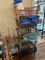 Five plastic stacking storage baskets stacked vertically in colors including pink, beige, and black with folded plastic tablecloths placed inside and on top.