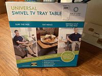 Photo of unopened original box of Universal Swivel TV Tray Table showing product name, brand, and promotional use images.
