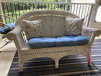Full view of the white wicker loveseat showing cushion and pillows on covered porch.