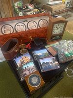 Full lot display including watch winder, handheld compass, Waterbury clock, men's leather card holders, mail holder, postcards, coin wrappers, and coasters on black table.
