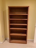 Full front view of tall wooden bookshelf with six shelves.