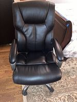 Front view of black leather office chair showing padded seat, back and armrests.