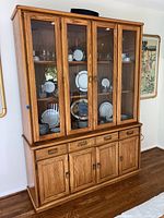 Front view of wooden two-piece china cabinet with glass doors displaying tableware inside and lower storage cabinet with drawers and doors.