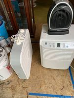 Photo showing all three appliances: Zenith dehumidifier, Pelonis table fan on top of the dehumidifier, and Lasko box fan nearby on the floor.