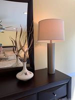 Table lamp and ceramic vase on a dark wooden surface next to a mirror.