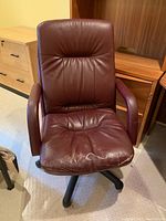 Front view of maroon leather swivel desk chair showing wear on seat and padded backrest with armrests