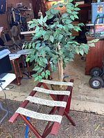 Wide view of the folding luggage rack with the faux tree placed behind it in a workshop or garage setting.