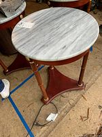 Round marble top end table showing overall top surface and part of wooden base with brass accents.