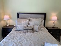 Pair of two matching lamps placed on either side of a bed with beige bedding, each lamp features a metal base and stem with a white shade.