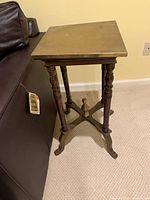Side table showing full height and base with carved wooden legs against a couch.