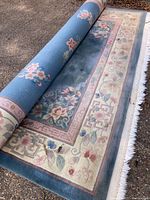 Top view of the partially rolled blue rug showing floral and geometric border designs on an outdoor surface.