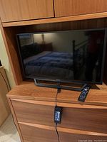Front view of the Sony Bravia television placed on wooden furniture, showing screen and remote control on the right side.
