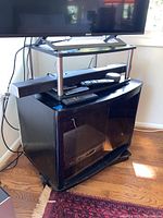 Full view of the television stand showing the swivel platform with a TV and remotes on it, and the black base cabinet with curved glass front doors.