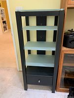 Front view of wood and glass shelf unit showing three frosted glass shelves and wooden bottom drawer with metal knob, set against a wall.