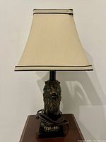 Front view of lamp showing lion head base and cream square shade with black trim