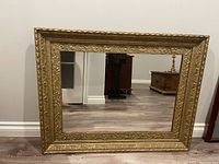 Front view of antique wall mirror showing rectangular shape and detailed gold ornate frame with floral and geometric embossing.