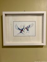 Framed art print of two stylized hummingbirds, white frame, behind glass