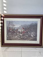 Framed art print entitled 'Run To The Earth' showing a hunting scene with riders on horseback and dogs, with reddish-brown frame and cream mat.