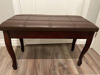 Front angle showing the brown faux leather padded top and wooden legs with curved design.