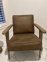 Front view of the chair showing brown faux suede seat and cushion with wooden frame and armrests.