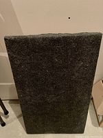 Top side of wooden dolly covered in dark gray carpeting, showing rectangular shape and texture.