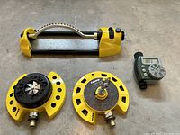 Three yellow Dramm sprinklers and one green programmable water timer placed on a concrete floor.