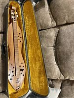 Top view of dulcimer inside open hard-shell case showing decorative sound holes and three strings.
