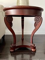 Front view of one Bombay Company wooden end table showing detailed carved legs and triangular shelf base