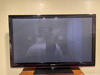 Samsung flat screen television showing the front view of the TV with black bezel and stand in a room with reflection