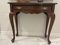 Front view of wooden hallway table showing drawer with brass handles and curved legs.