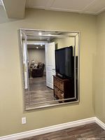 Rectangular modern wall mirror mounted on wall, showing reflective surface and decorative silver-tone frame.