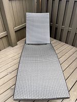 Dark brown woven rattan-style outdoor lounger with adjustable backrest in upright position on wood deck patio.
