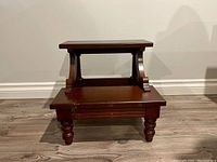 Front view of the two-step wooden stool showing structure, legs, and step surfaces with visible wear marks on lower step.