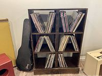 Photo of a wooden storage shelf containing LP vinyl records in six compartments. Shelf is dark stained wood.