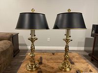 Front view of the pair of brass table lamps with black metal shades on wooden table.