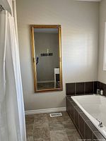 Full length wall mirror with an ornate gold frame mounted on a pale wall next to a bathtub and a shower curtain.