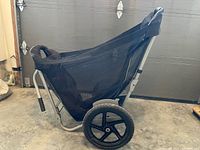 Side view of the yard wagon showing the black mesh cargo area supported by a silver metal frame and a large black wheel with 5 spokes.