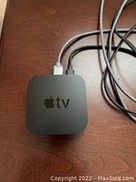 Overhead view of Apple TV 4K device with connected power and HDMI cords on a wood surface.