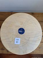 Top view of a round wooden balance board with a Fitter First blue and yellow logo sticker in the center.