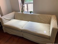 Side angle view of large cream/white sofa showing removable cushions, fabric cover, and signs of wear