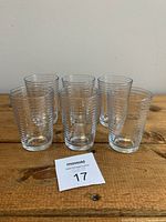 Six small clear drinking glasses with horizontal line texture arranged in rows on a wooden surface.