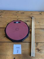 Top-down view of the 8.5-inch drum practice pad and two wooden drumsticks on a wooden surface.